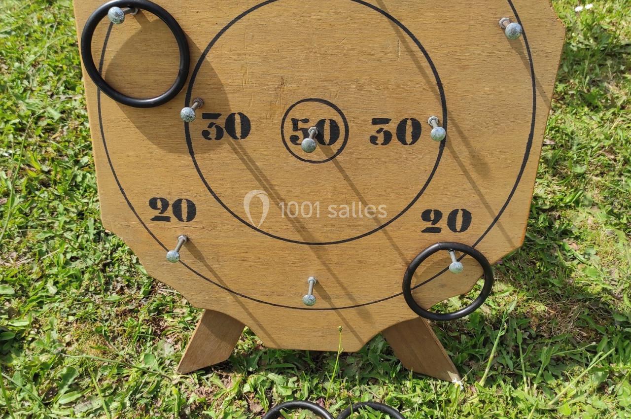 Cible en bois avec des anneaux noirs posés dessus et au sol, installée sur une pelouse.