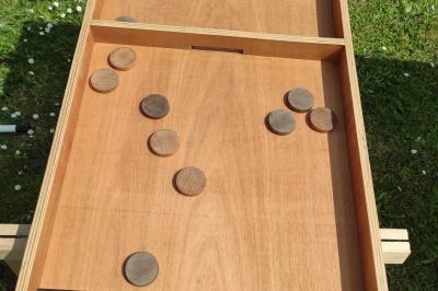 Planche de jeu de lancer de sacs colorée posée sur une pelouse, avec des sacs verts et jaunes dispersés autour.