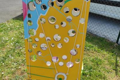 Planche de jeu de lancer de sacs colorée posée sur une pelouse, avec des sacs verts et jaunes dispersés autour.