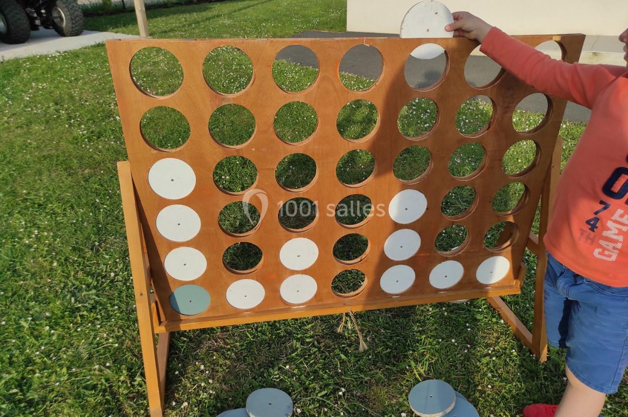 Un enfant joue à un grand jeu de puissance 4 en bois dans un jardin, tenant un jeton blanc.