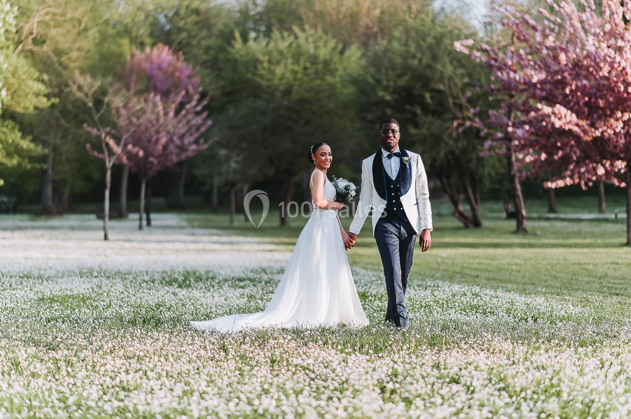 Un couple en tenue de mariage marche main dans la main dans un parc fleuri au printemps.