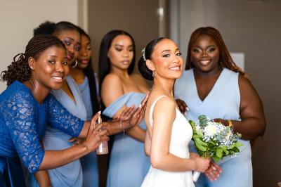 Un couple de mariés pose près d'une voiture ancienne blanche devant un bâtiment historique et des arbres.