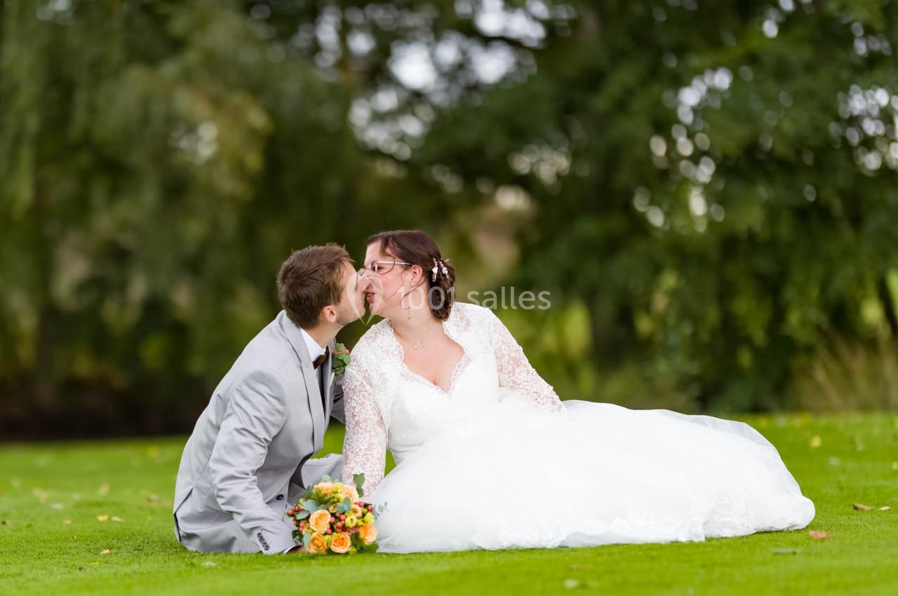 Un couple de mariés assis sur l'herbe, s'embrassant, avec un bouquet de fleurs posé à côté d'eux.