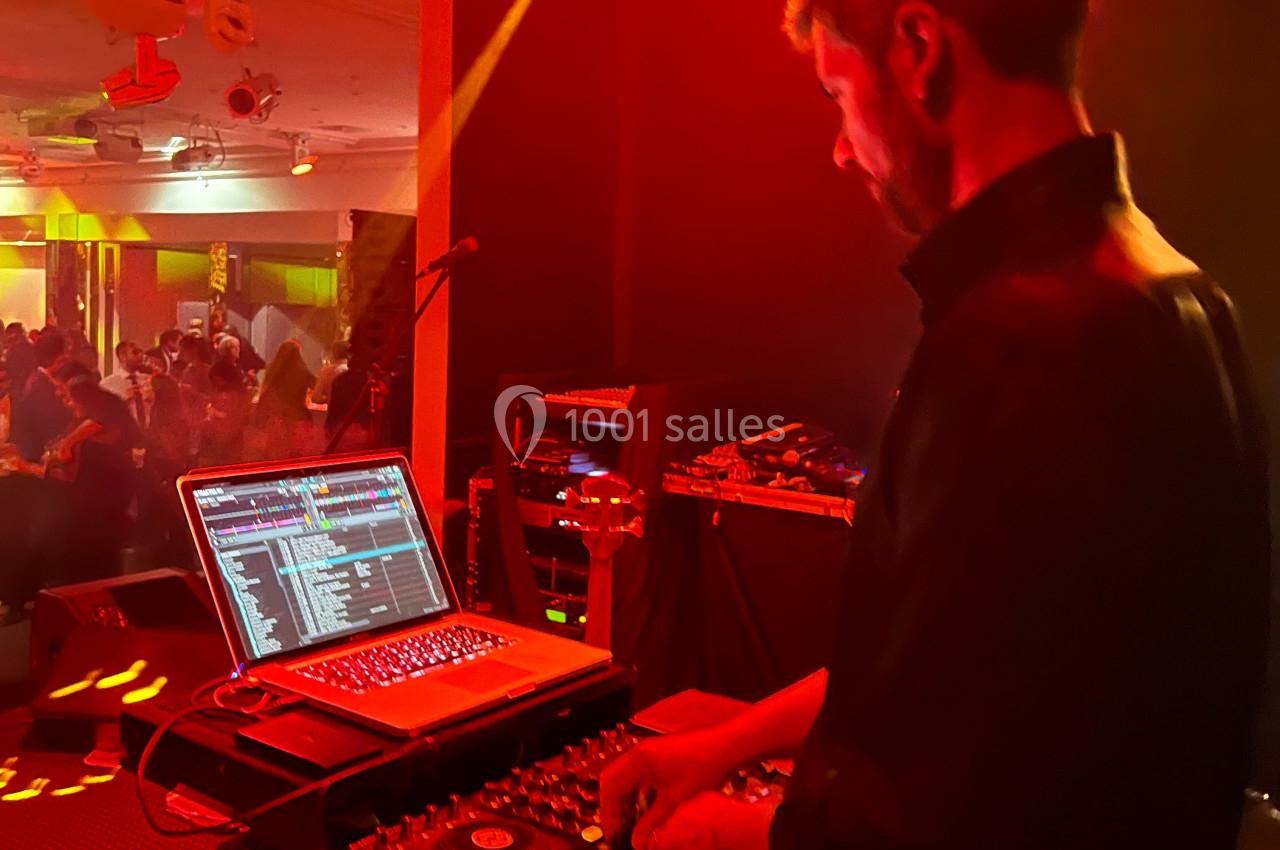 Un DJ mixe de la musique sur un ordinateur portable et une table de mixage dans une salle éclairée de lumières rouges.