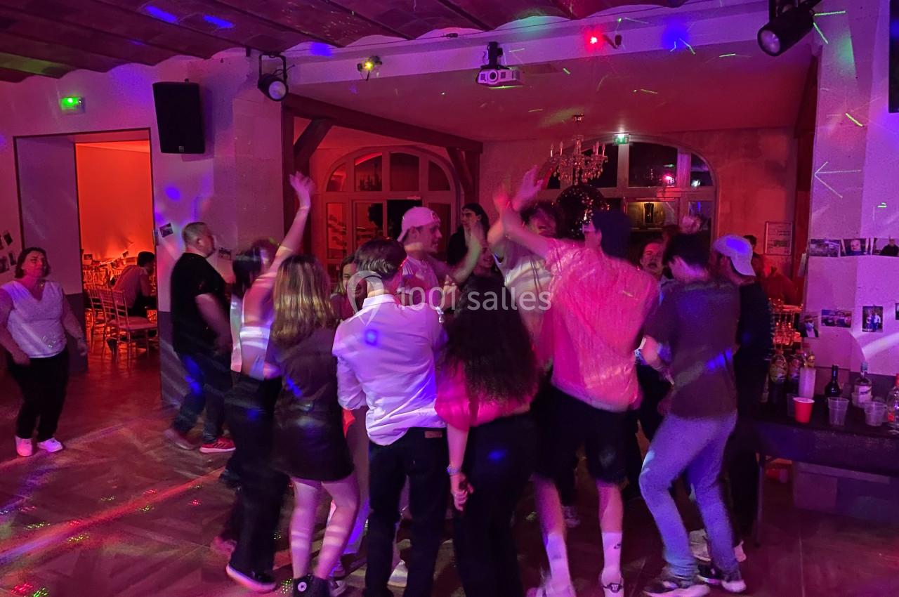 Groupe de personnes dansant sous des lumières colorées dans une salle avec un plafond en bois.