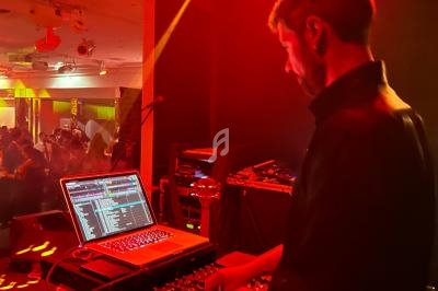 Un DJ mixe de la musique sur une console devant un public dans une ambiance lumineuse rouge et jaune.