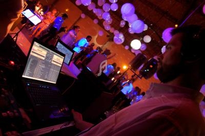 Un DJ utilise un ordinateur portable pour mixer de la musique lors d'une soirée avec des lumières et des invités dansants.