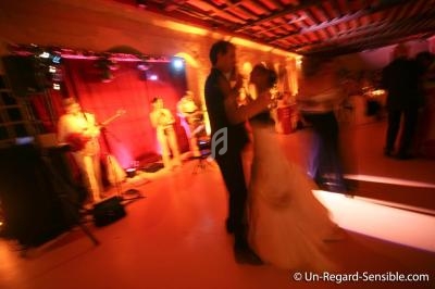 Un couple danse dans une salle éclairée de lumières chaudes, avec un groupe de musiciens en arrière-plan.