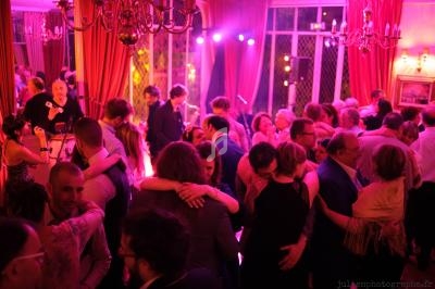 Des personnes dansent et discutent dans une salle éclairée par des lumières colorées, avec un groupe en arrière-plan.