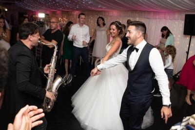 Un couple de mariés danse entouré d'invités sous un plafond illuminé, avec un saxophoniste jouant en direct.