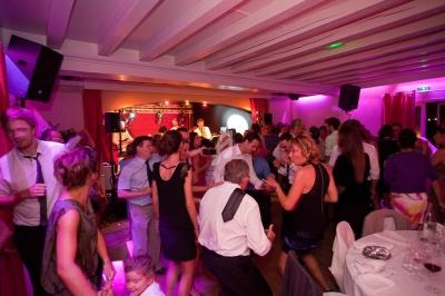 Des personnes dansent et discutent dans une salle éclairée par des lumières colorées, avec un groupe jouant sur scène.