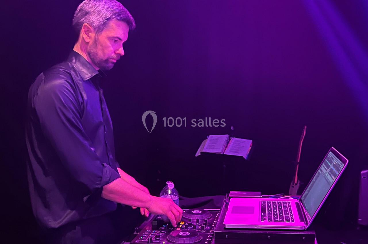Un DJ mixant de la musique sur une table de mixage, éclairé par une lumière violette dans un environnement sombre.