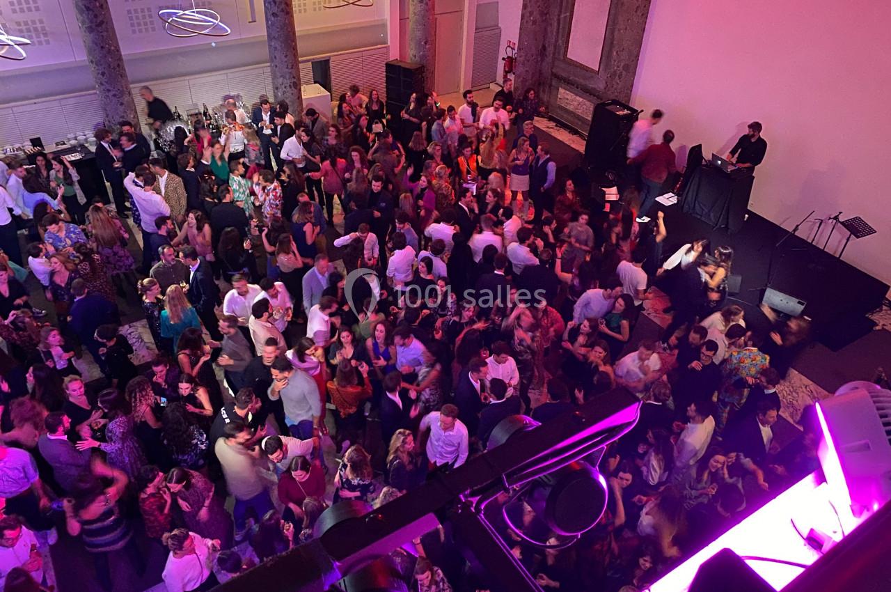 Salle bondée avec des personnes dansant et socialisant lors d'un événement festif, éclairée par des lumières colorées.
