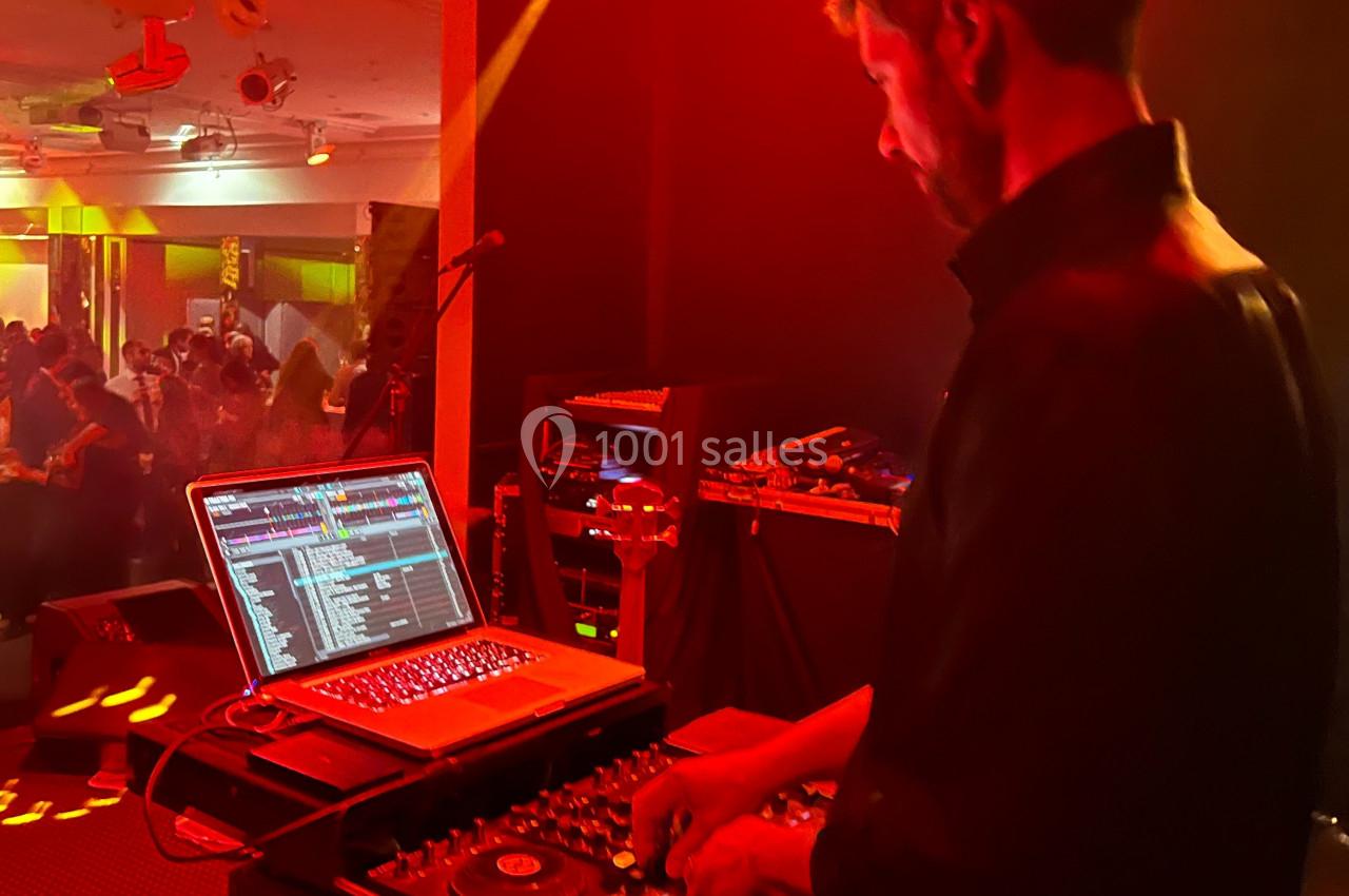 Un DJ mixe de la musique sur une console avec un ordinateur portable, éclairé par des lumières rouges, devant une foule.
