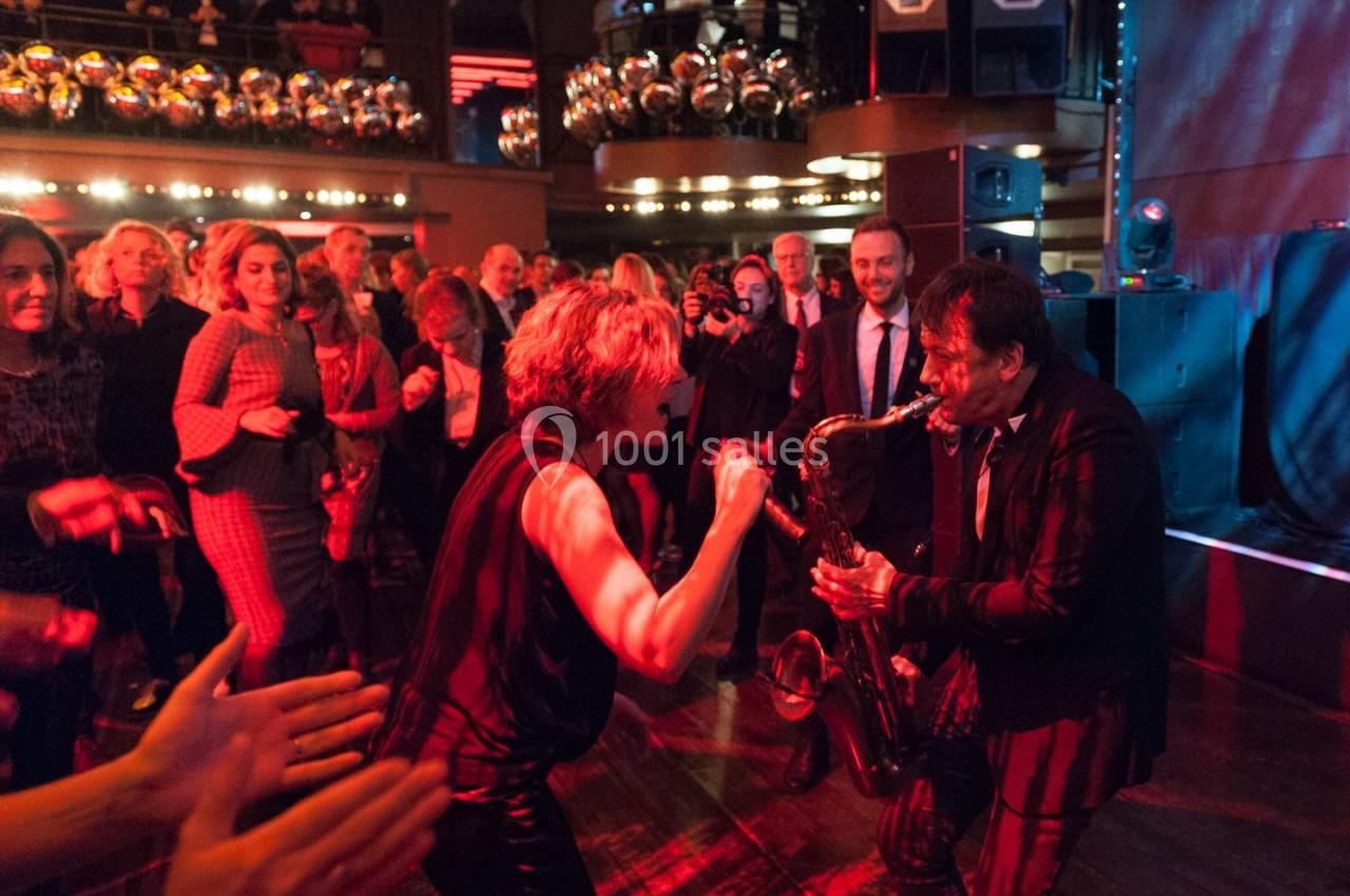 Deux musiciens jouent au milieu d'une foule dans une ambiance festive et éclairée par des lumières rouges.