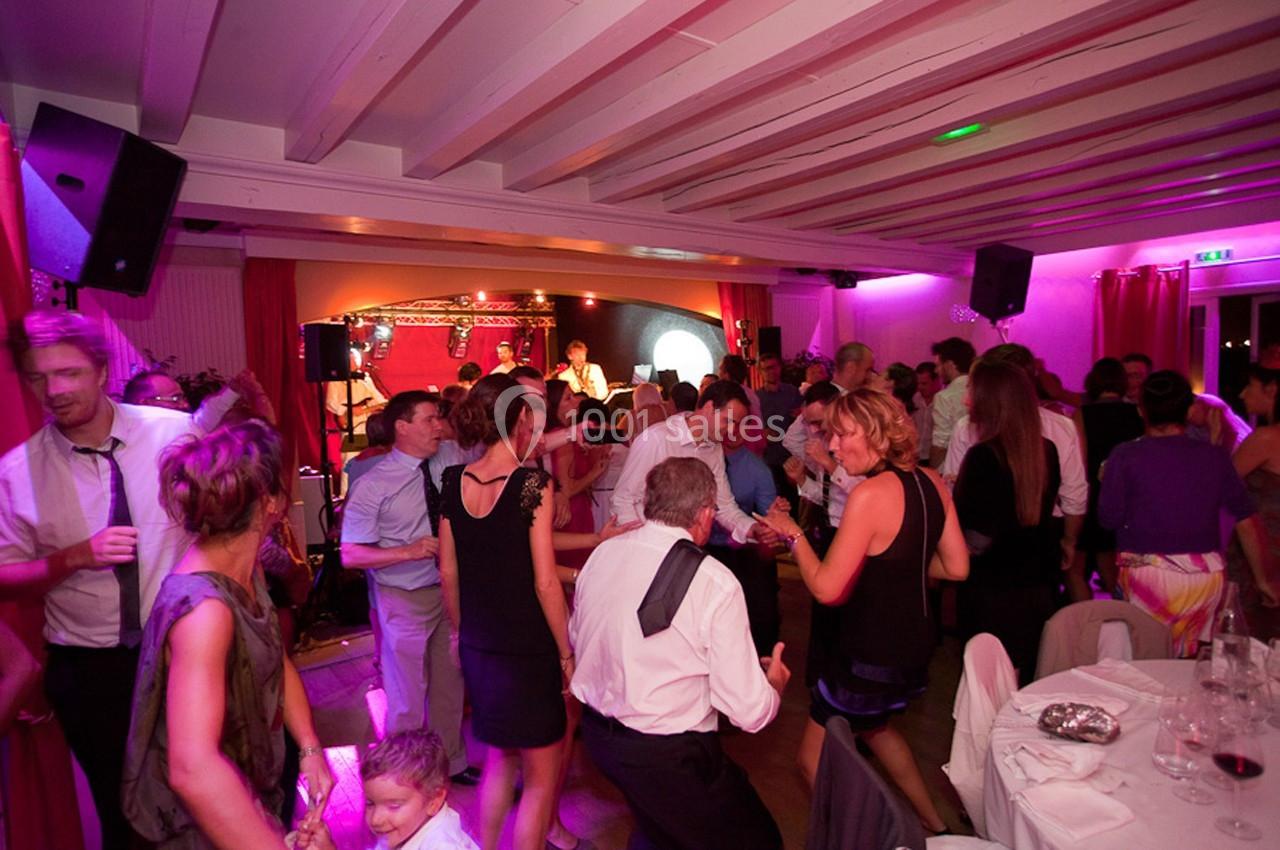 Des personnes dansent et discutent dans une salle éclairée par des lumières colorées, avec un groupe jouant sur scène.