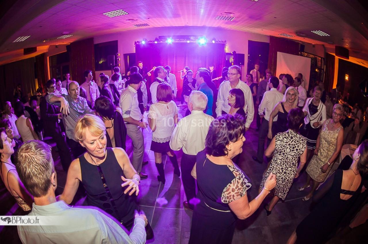 Des personnes dansent et discutent dans une salle éclairée par des lumières colorées lors d'un événement festif.