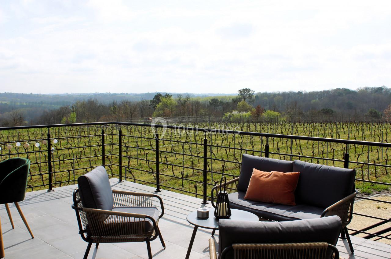 Terrasse aménagée avec mobilier d'extérieur, offrant une vue dégagée sur des vignes et un paysage naturel.