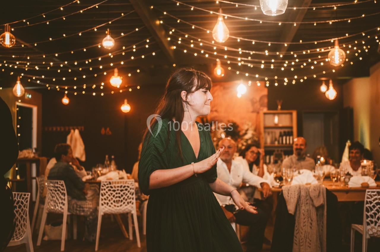 Une femme en robe verte danse dans une salle décorée de guirlandes lumineuses, entourée de convives assis.