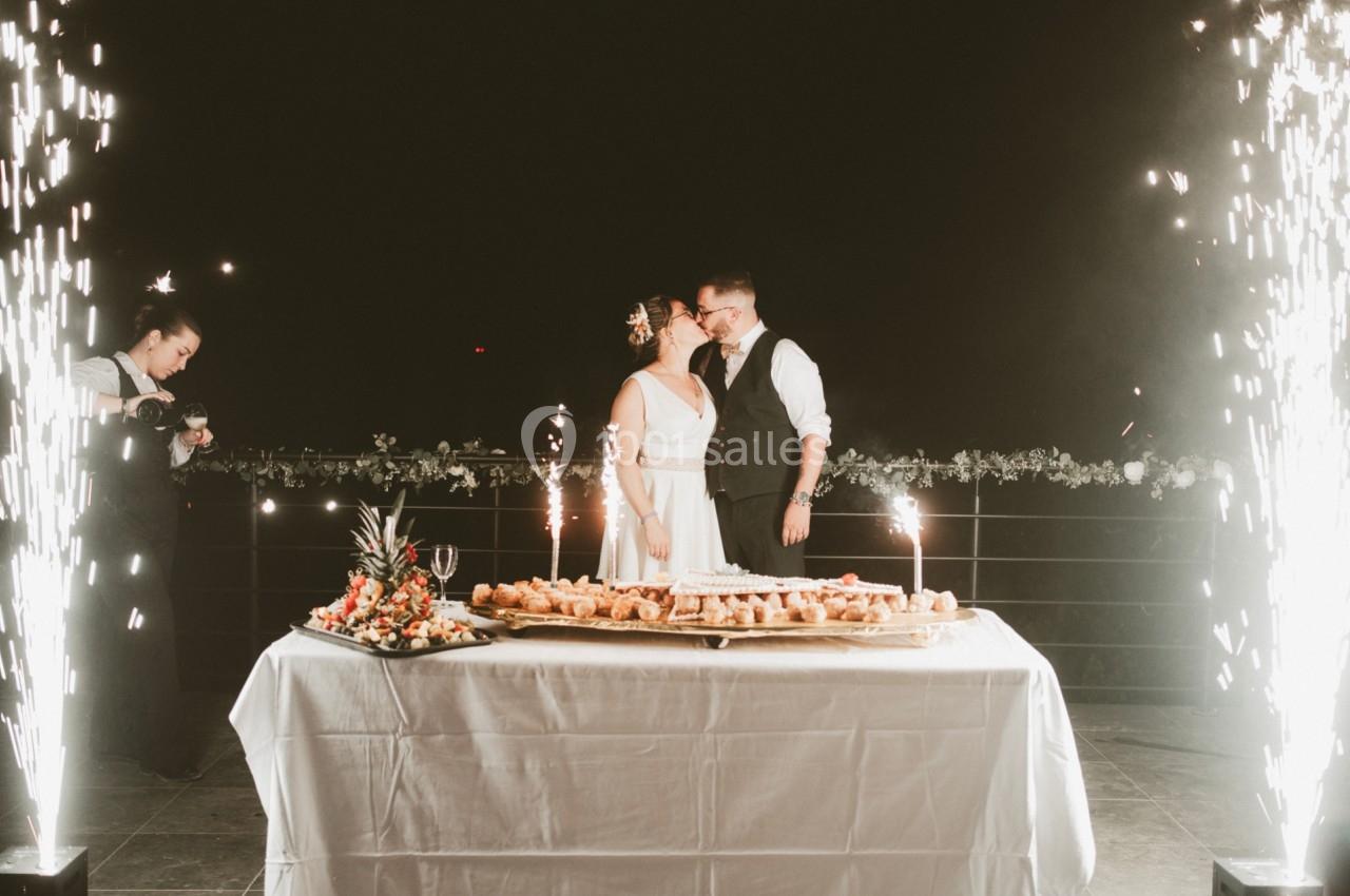 Un couple en tenue de mariage s'embrasse devant une table garnie, entouré de gerbes d'étincelles.