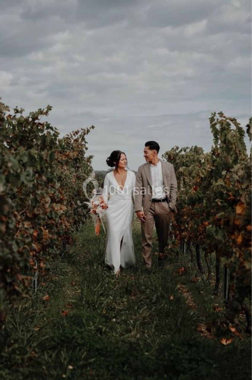 Location salle Saint-Genès-de-Lombaud (Gironde) - Domaine du Château Icla #5 Un couple marche main dans la main dans un vignoble sous un ciel nuageux.