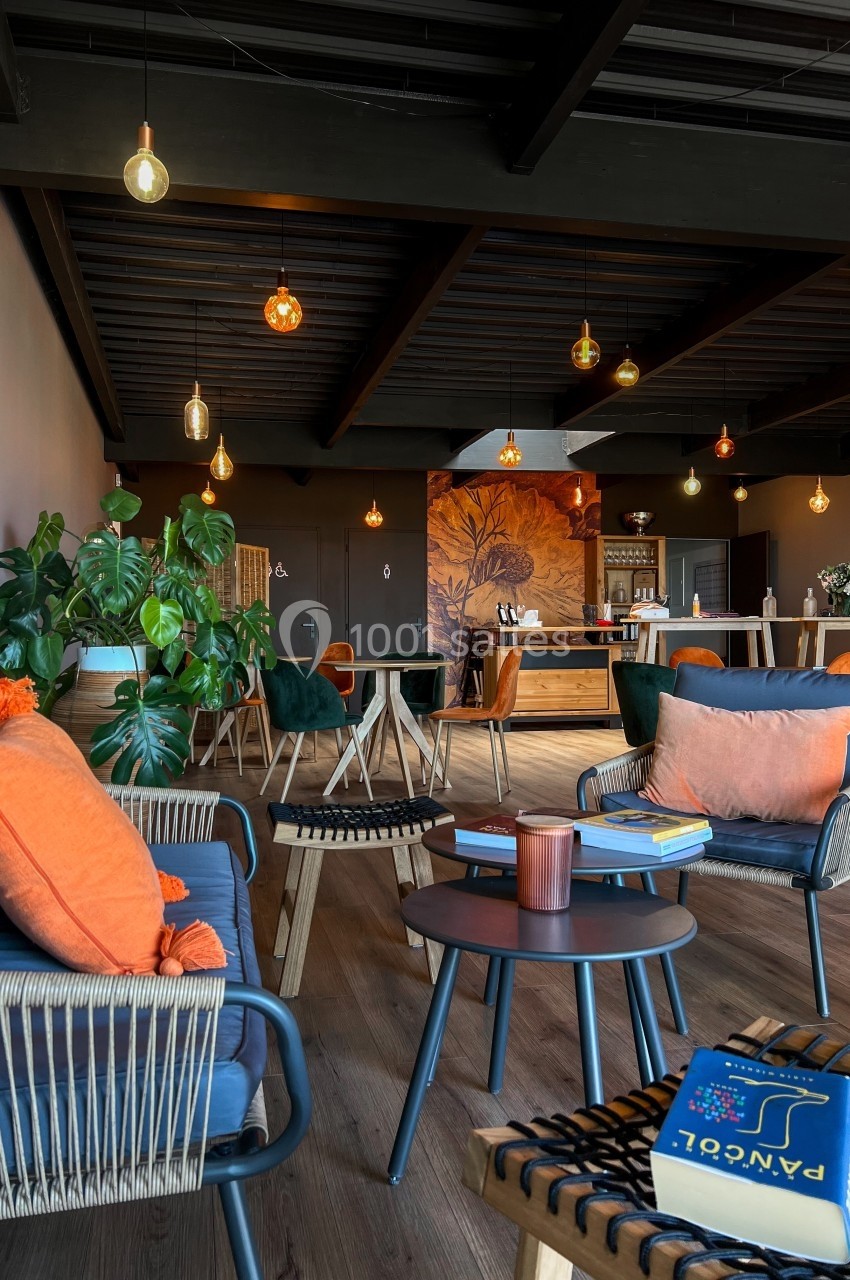 Location salle Saint-Genès-de-Lombaud (Gironde) - Domaine du Château Icla #11 Espace de détente moderne avec fauteuils en rotin, tables basses, plantes et éclairage suspendu chaleureux.