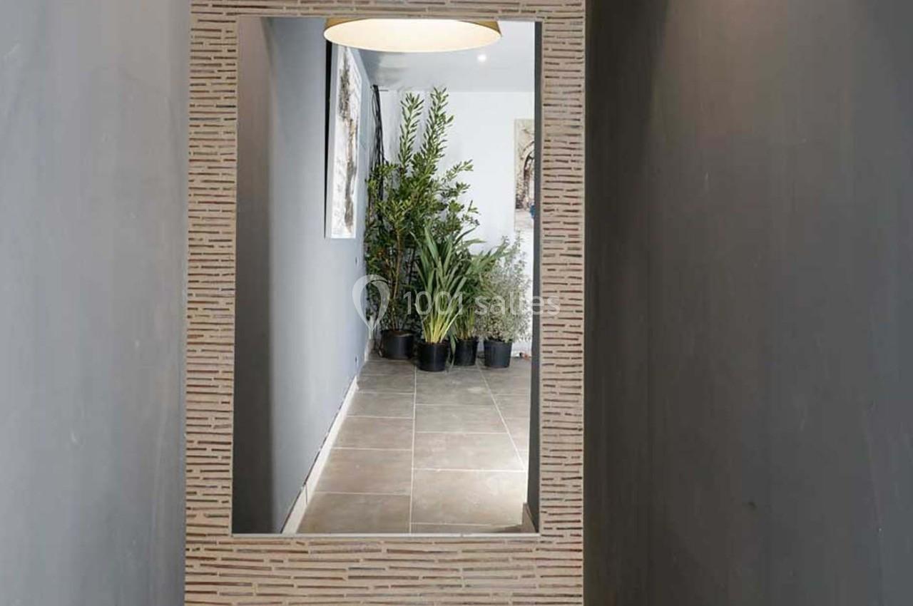 Grand miroir encadré reflétant un couloir gris avec des plantes vertes en pots au fond.