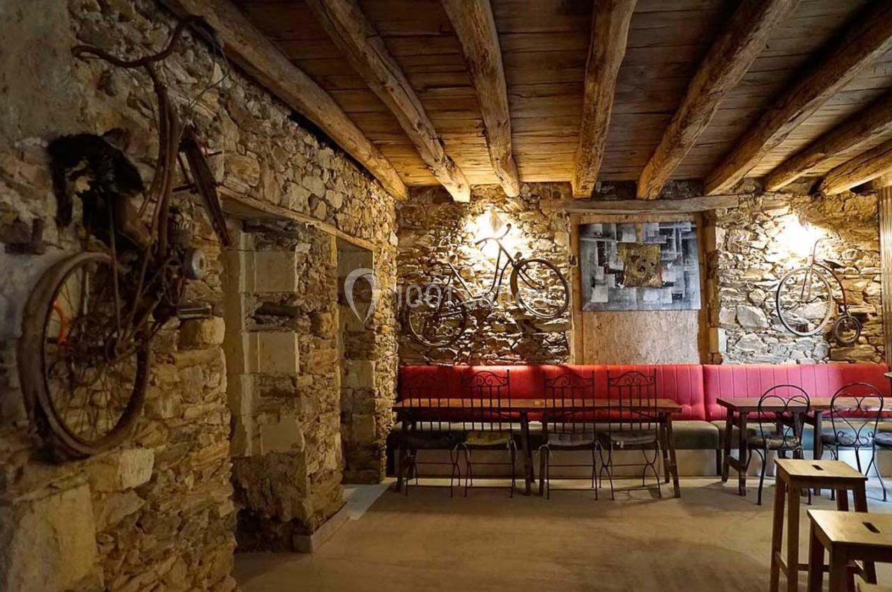 Salle rustique avec murs en pierre, plafond en bois, vélos accrochés et mobilier en métal et bois.
