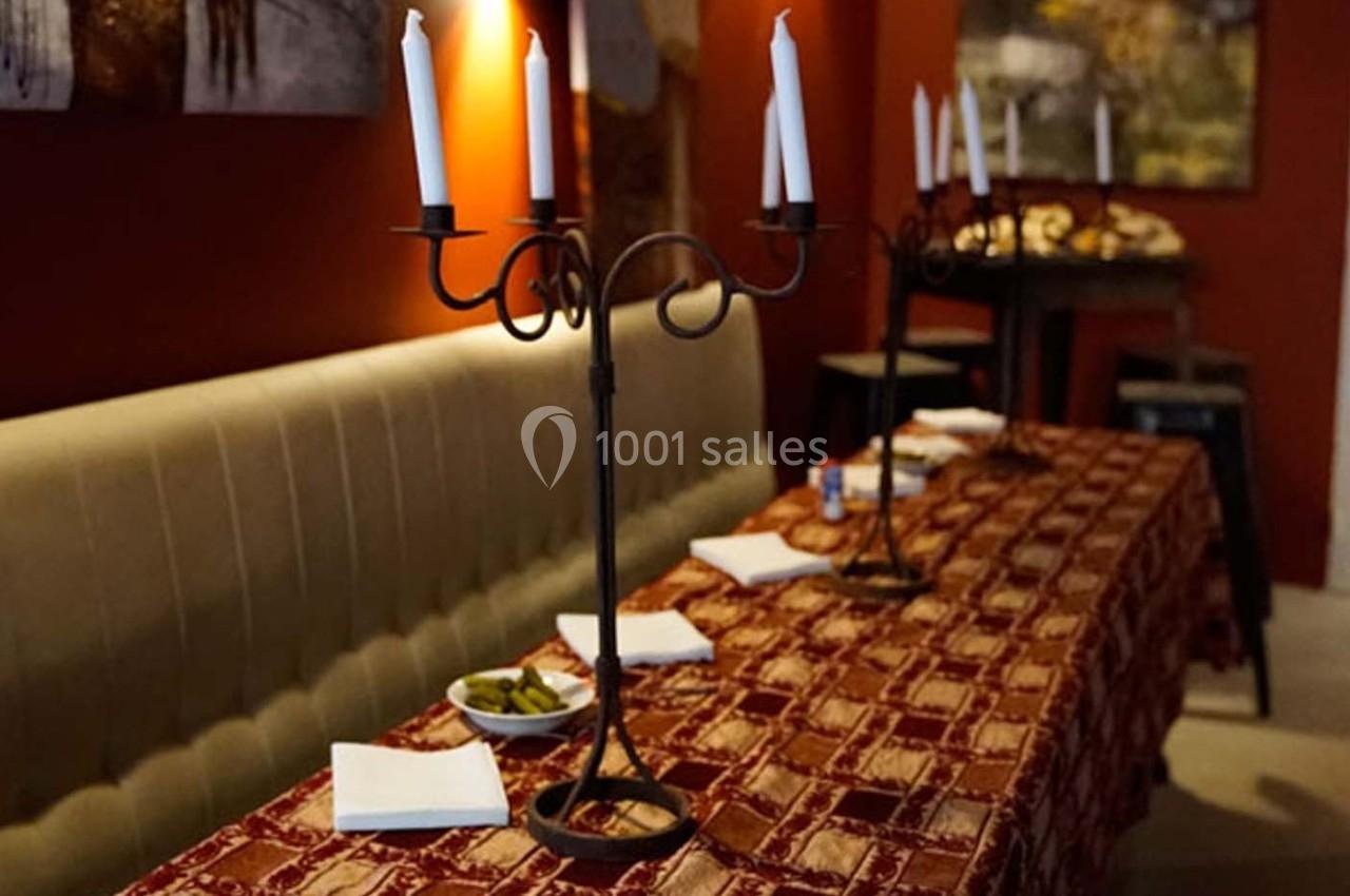 Deux chandeliers à bougies décorent une table recouverte d'une nappe rouge dans un intérieur chaleureux.