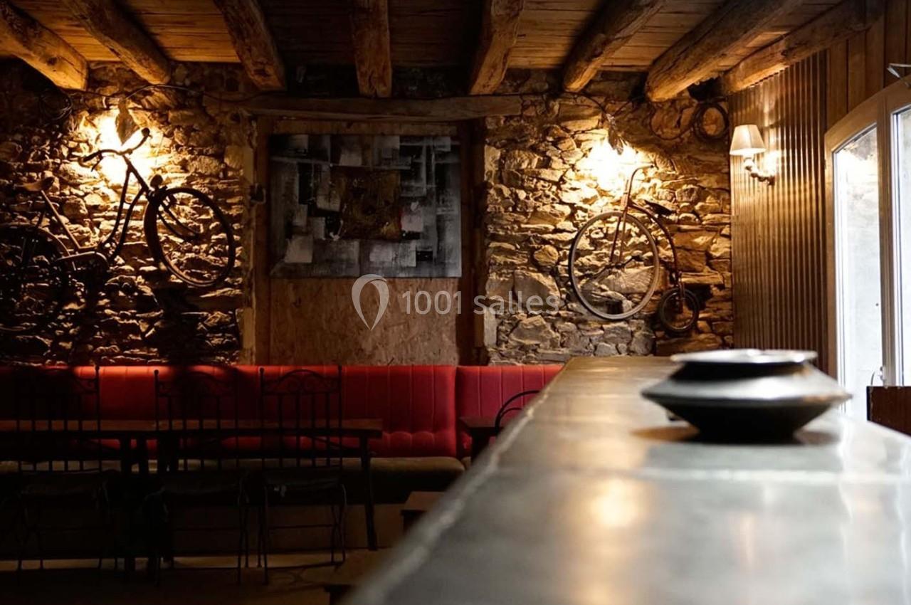 Intérieur rustique avec murs en pierre, vélos accrochés, banquettes rouges et éclairage chaleureux.