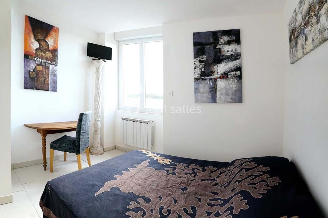 Chambre lumineuse avec un lit, une table en bois, une chaise, des tableaux abstraits et une fenêtre donnant sur l'extérieur.