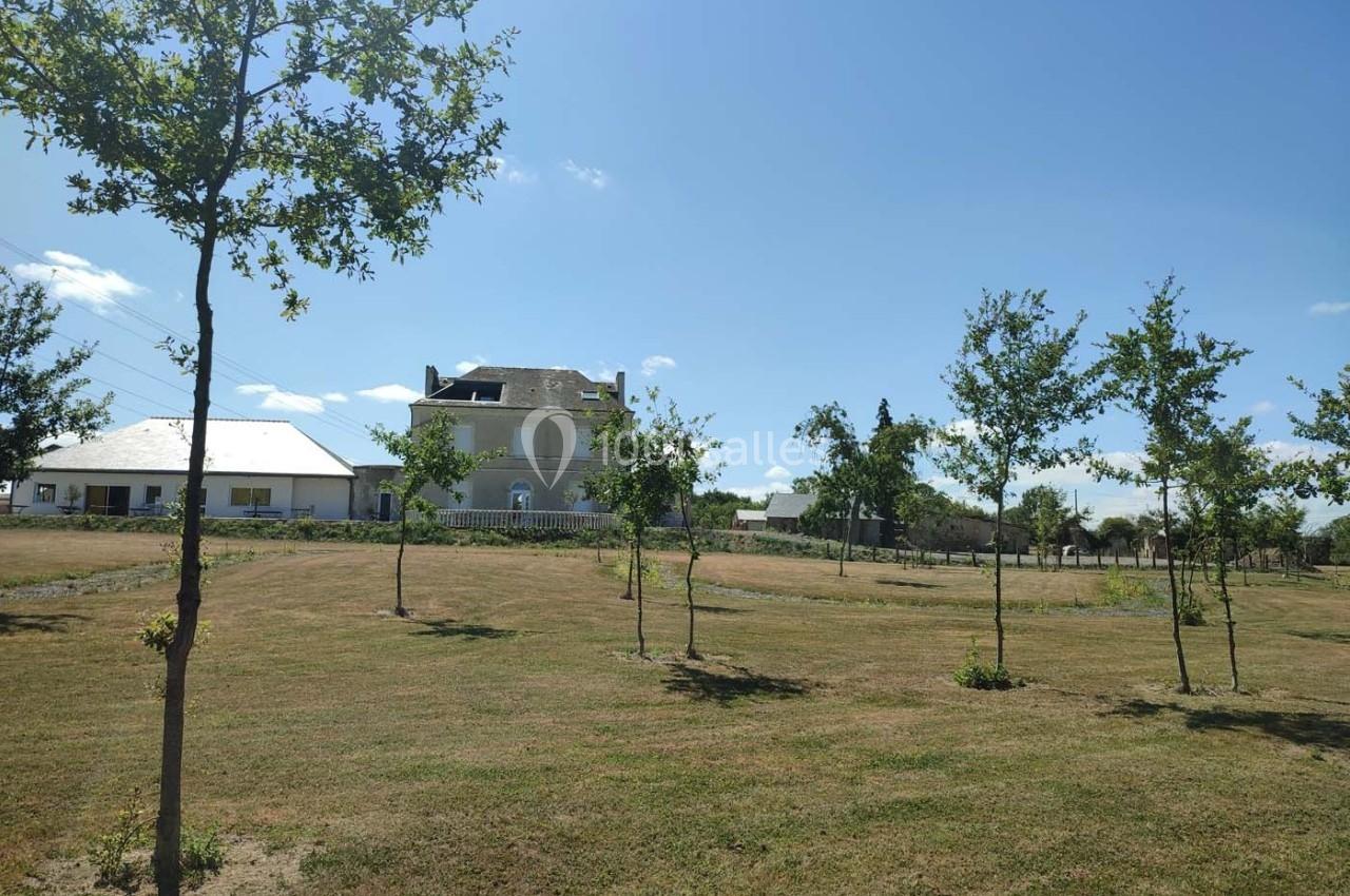 Maison en pierre entourée d'un grand jardin avec des jeunes arbres sous un ciel bleu dégagé.