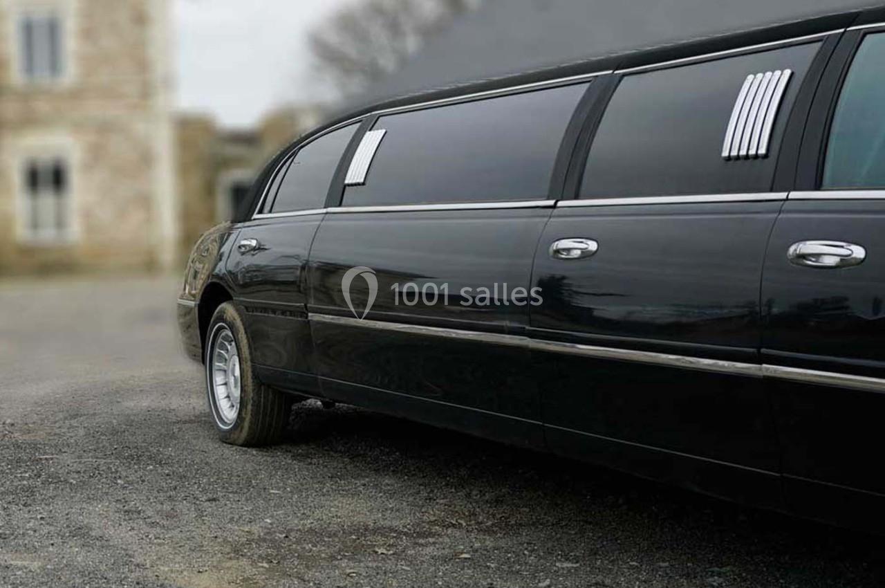 Limousine noire stationnée sur une allée en gravier, avec un bâtiment en pierre flou en arrière-plan.