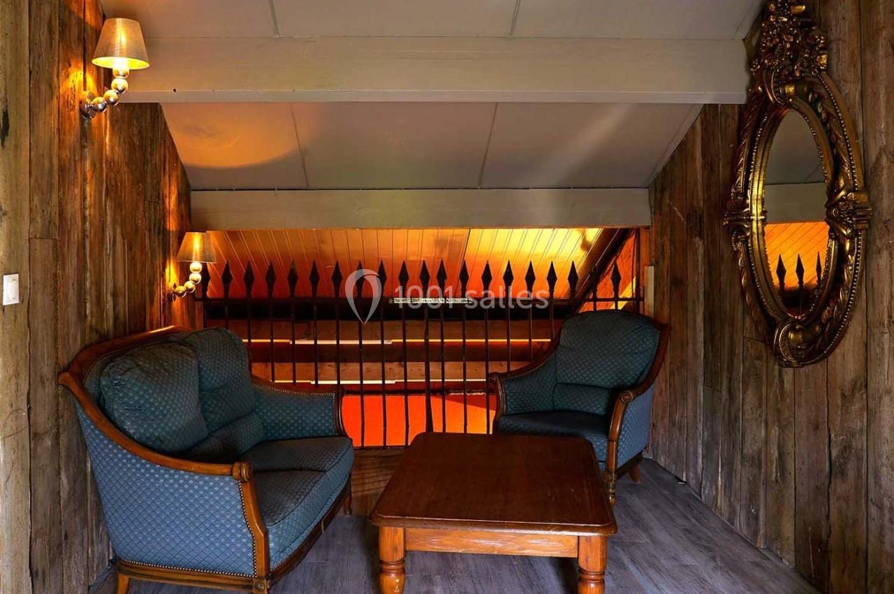 Deux fauteuils et une table basse en bois dans un espace rustique avec murs en bois, miroir doré et éclairage chaleureux.