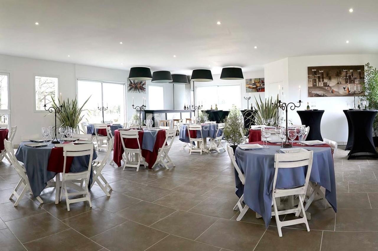 Salle de réception lumineuse avec tables dressées, nappes colorées et décorations végétales.