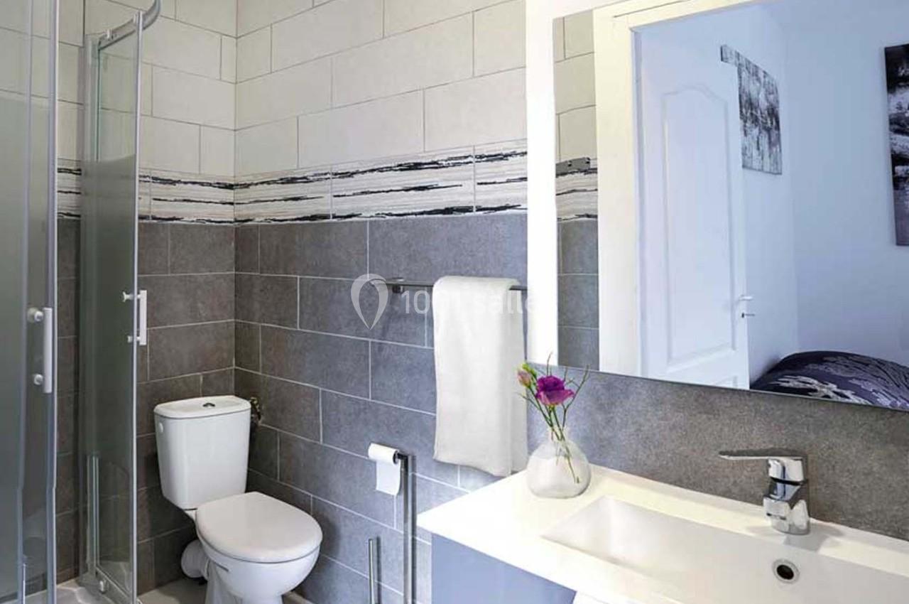 Salle de bain moderne avec douche vitrée, toilettes, lavabo blanc et décoration murale en carrelage gris et blanc.