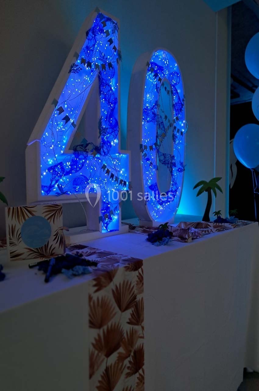 Décoration lumineuse avec le chiffre 40 éclairé en bleu, entouré de motifs tropicaux et de petits accessoires festifs.