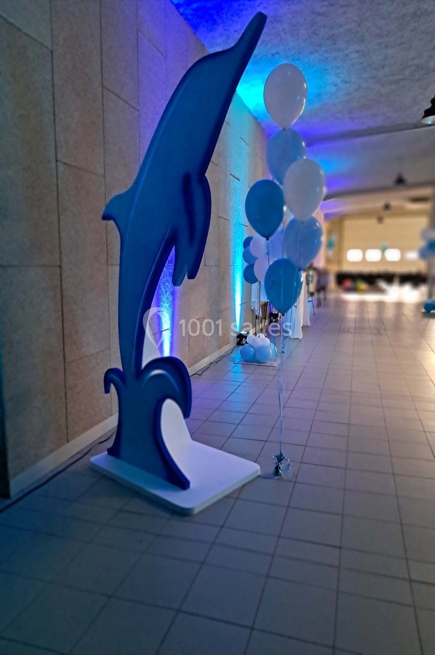 Statue de dauphin bleu et bouquet de ballons dans un couloir éclairé par des lumières bleues.