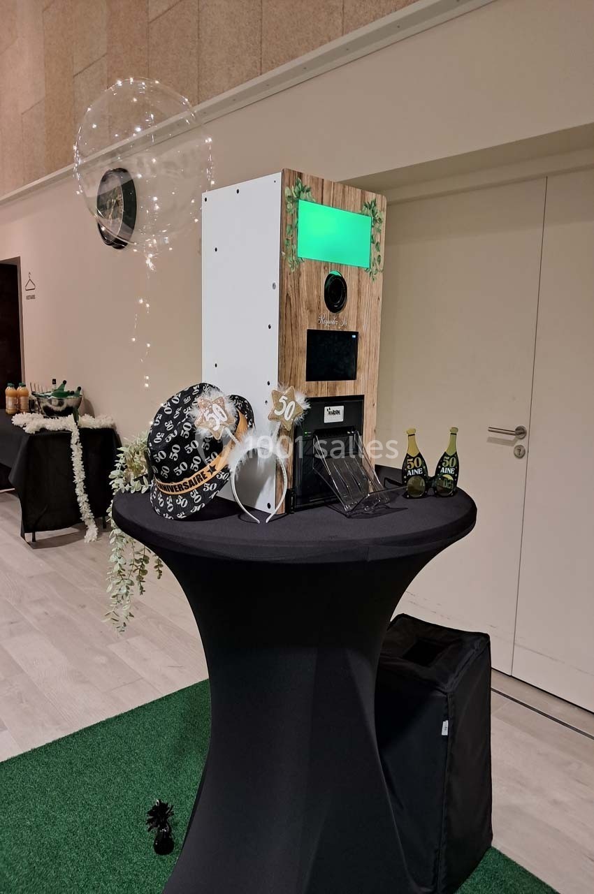 Borne photo sur une table haute décorée pour un événement, avec ballons et accessoires sur le thème des 50 ans.
