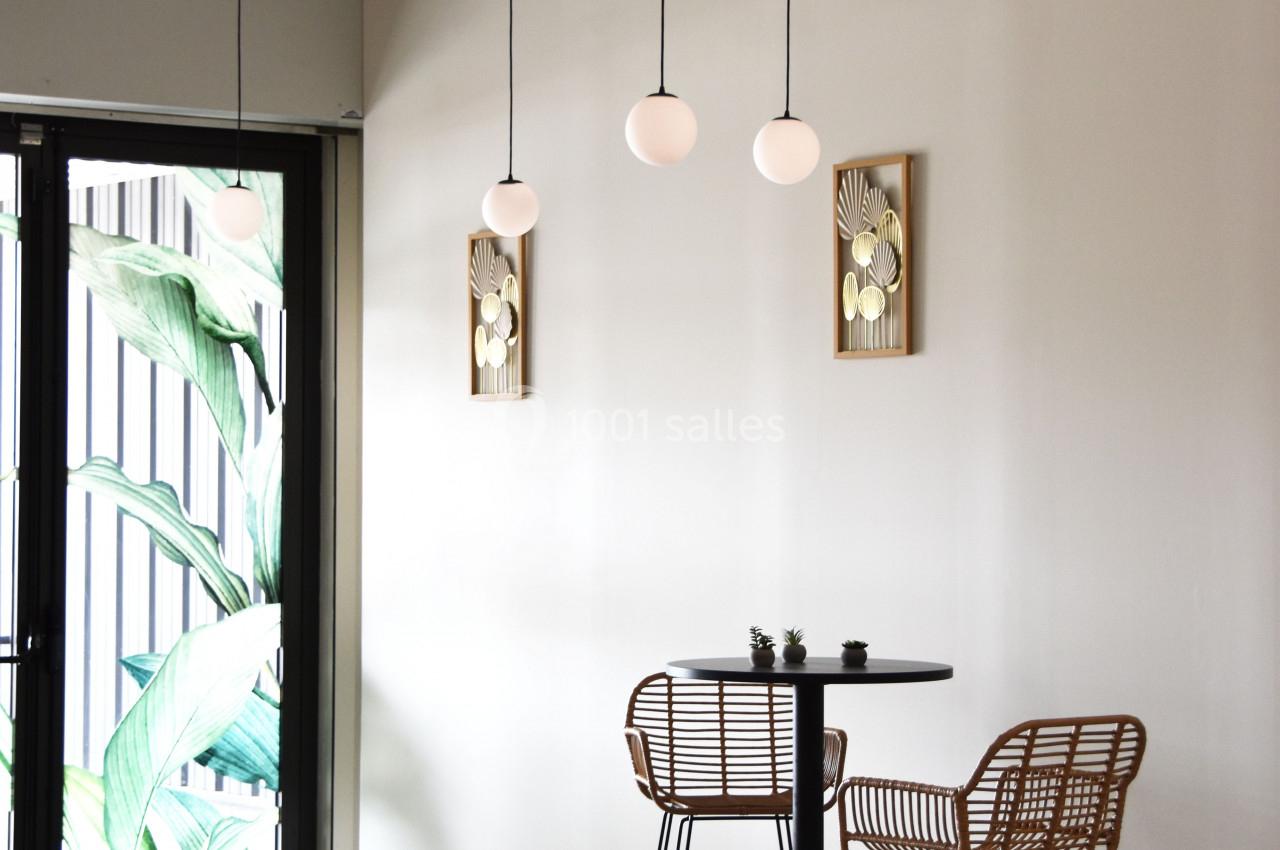 Deux chaises en rotin et une table haute noire dans un intérieur minimaliste avec des suspensions et des décorations murales.