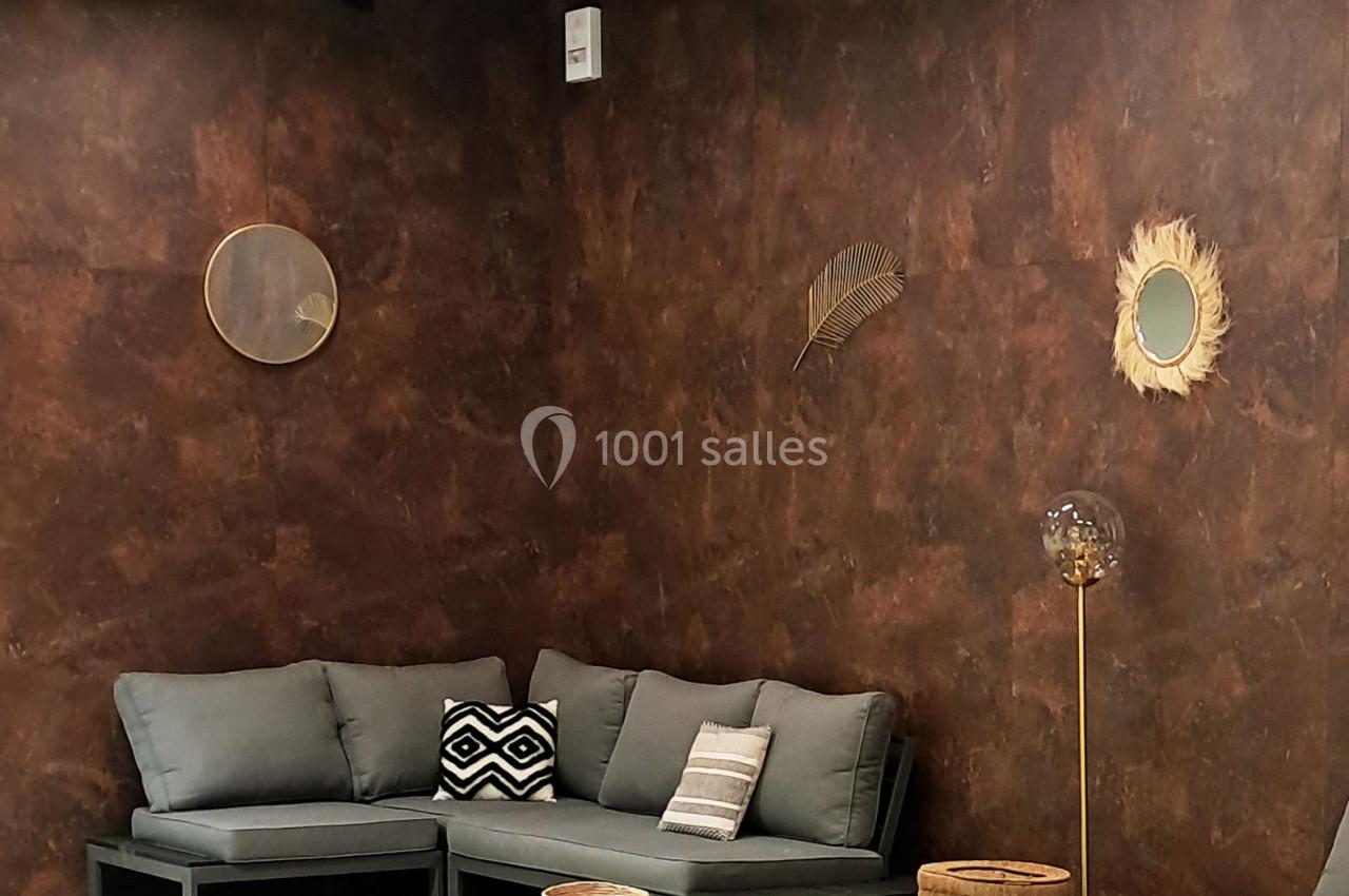 Espace salon avec canapés gris, tables basses noires, tapis en jute, murs marron et décorations murales naturelles.