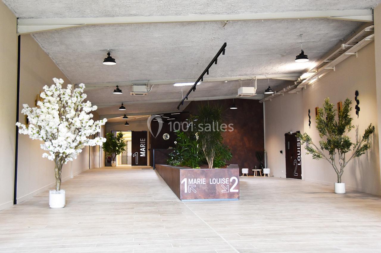 Entrée d'un espace intérieur moderne avec des plantes décoratives, un sol clair et un panneau indiquant deux directions.