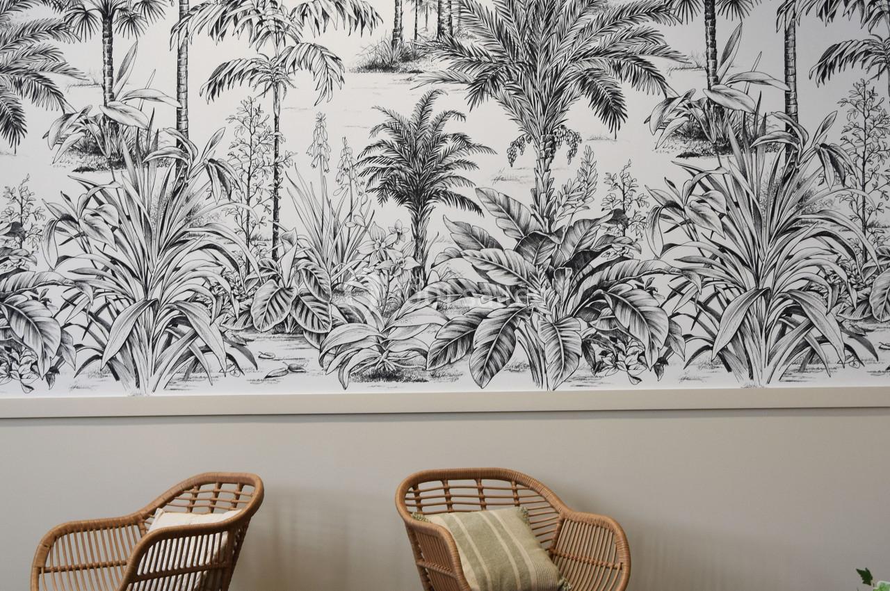 Deux fauteuils en rotin et une table basse en bois devant un mur décoré d'une fresque de palmiers en noir et blanc.