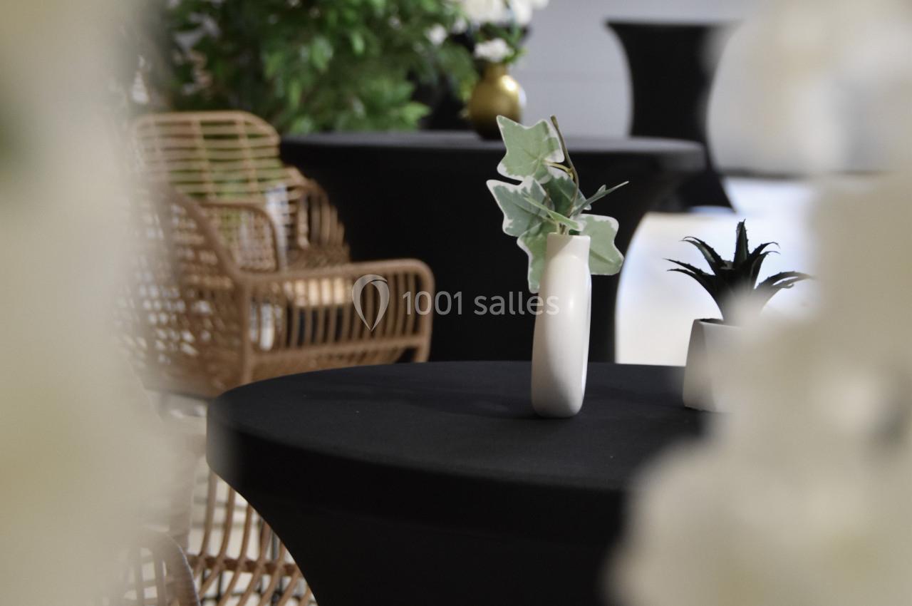 Tables hautes noires décorées de vases blancs et entourées de chaises en rotin dans un espace lumineux.