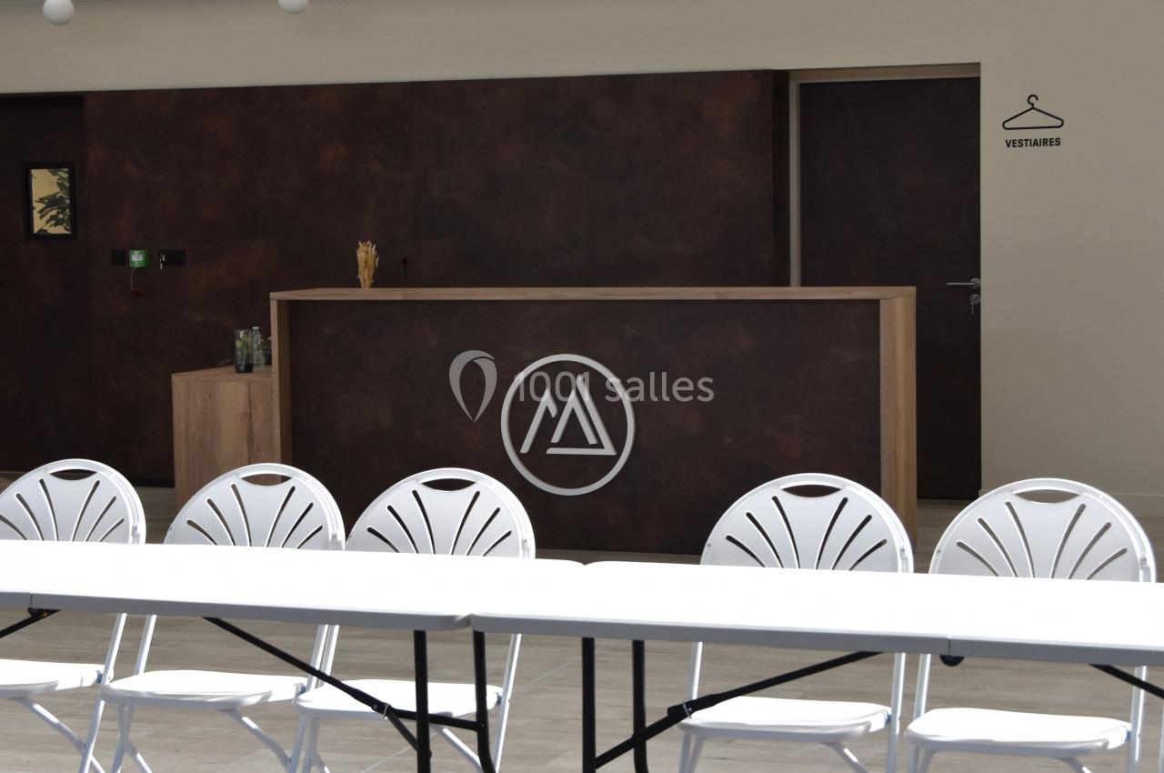 Salle lumineuse avec un comptoir en bois foncé, logo circulaire blanc, table et chaises blanches au premier plan.