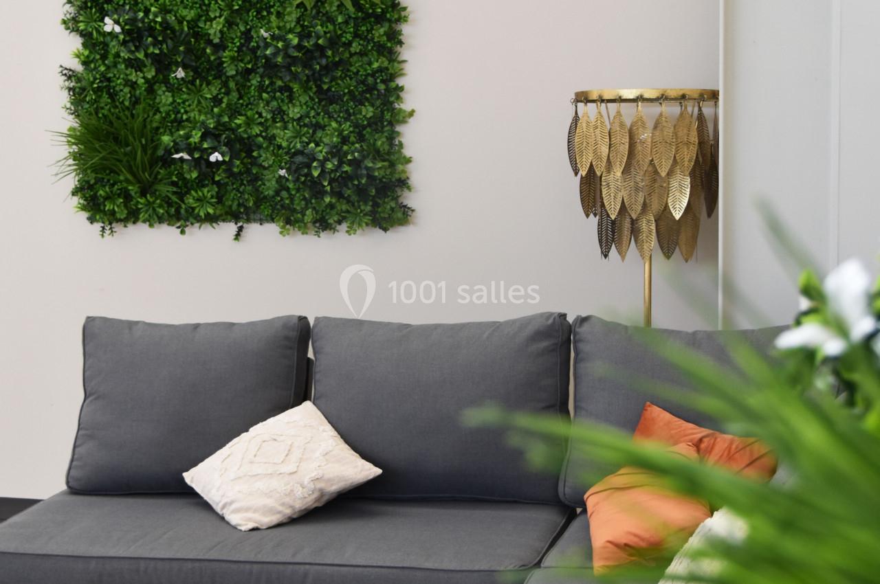 Canapé gris avec coussins colorés, table basse noire et mur végétal décoratif dans un espace intérieur lumineux.