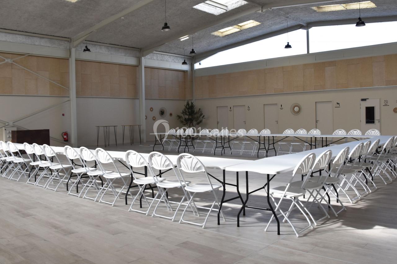 Salle lumineuse avec tables disposées en U et chaises blanches alignées, prête pour une réunion ou un événement.