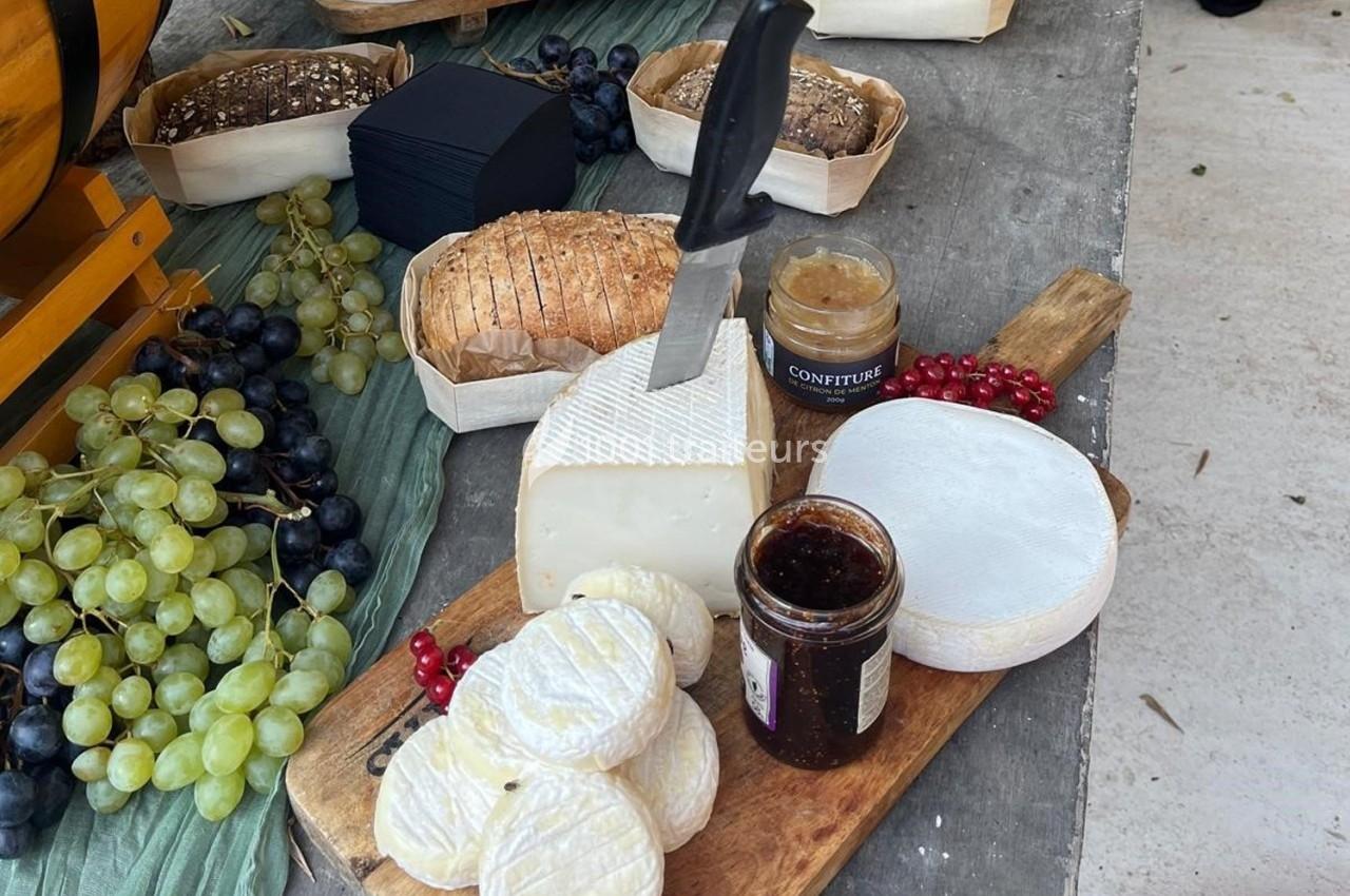 Plateau de fromages variés avec pain, raisins, confiture et couteau sur une planche en bois.
