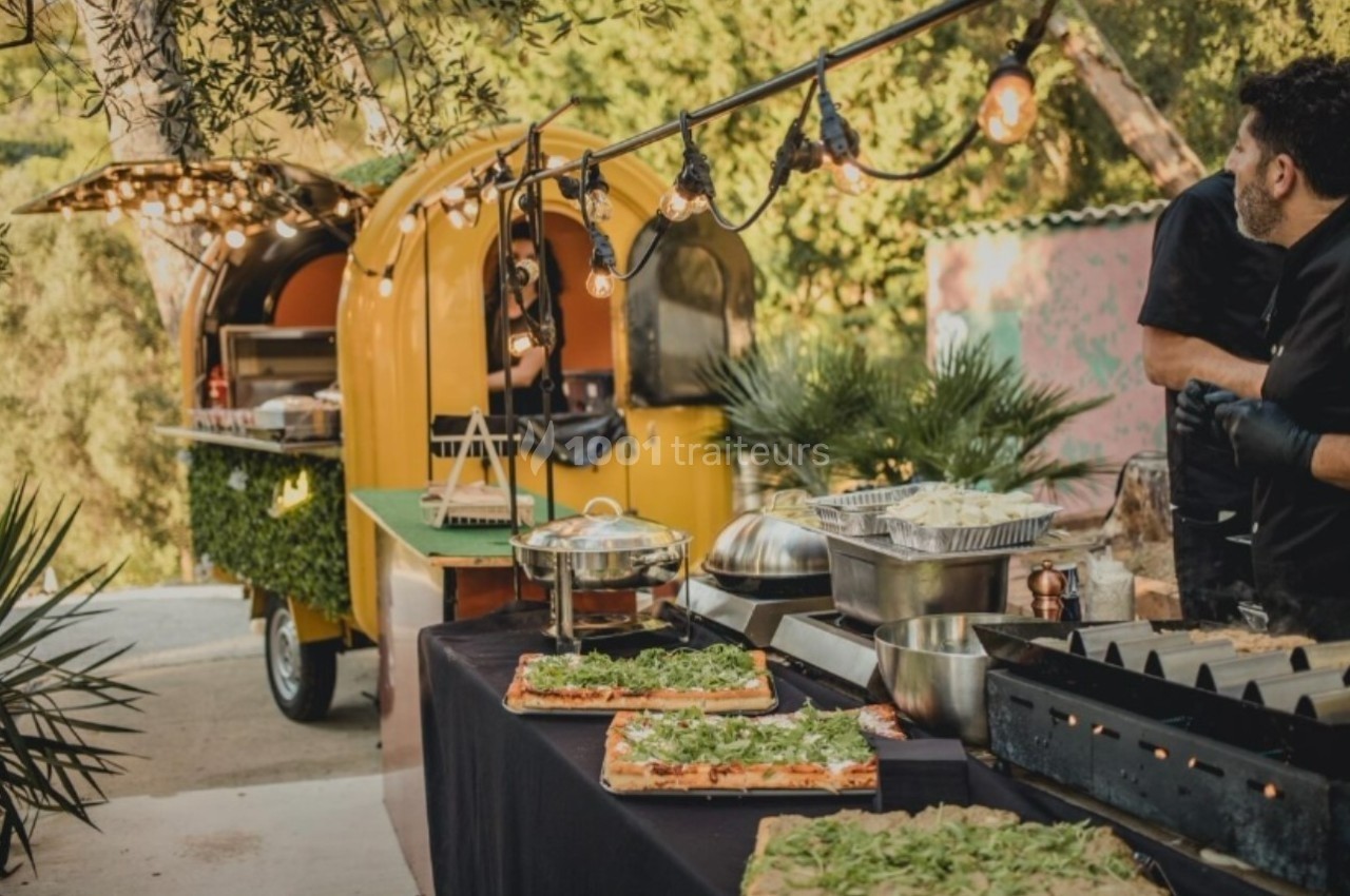 Food truck jaune avec guirlandes lumineuses, buffet de plats préparés et décoration végétale en extérieur.