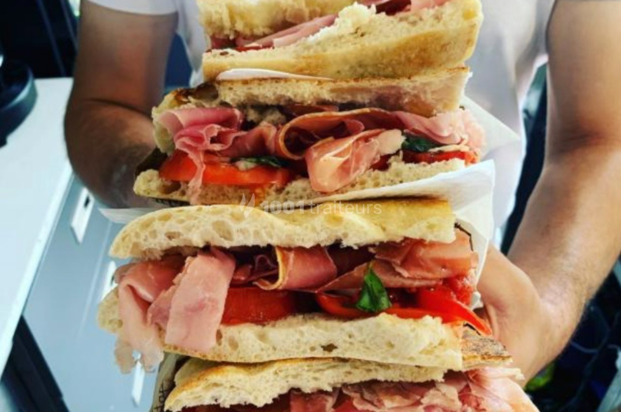 Sandwichs garnis de jambon, tomates et basilic, empilés et tenus à deux mains.